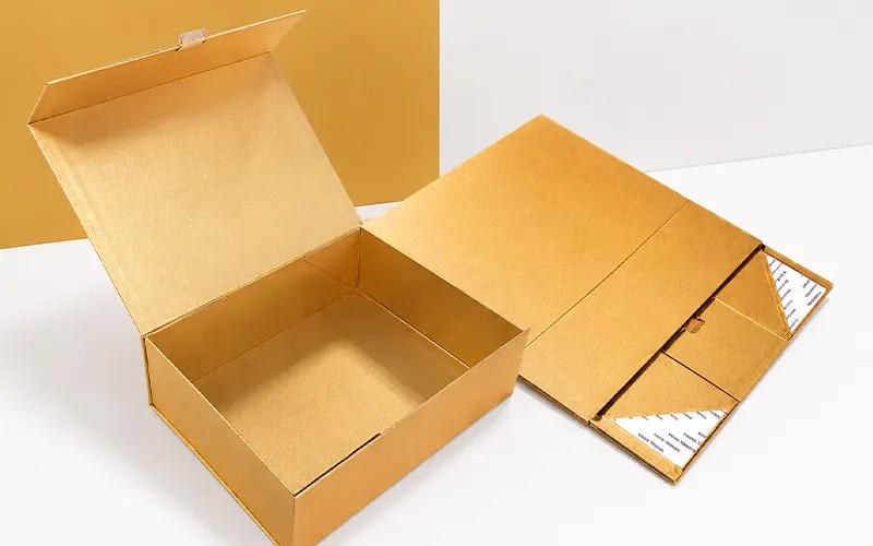 Open gold collapsible rigid box beside a folded blank